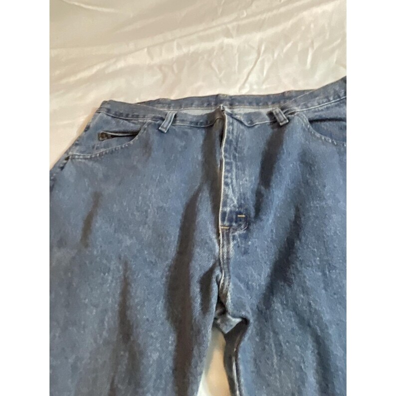 May include: Blue denim jeans with a classic five-pocket design. The jeans have a button and zipper closure, belt loops, and a relaxed fit. The denim has a medium wash with subtle fading.
