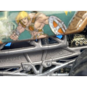 May include: A Hot Wheels monster truck toy featuring a cartoon image of a muscular character with blonde hair, a shield, and armor. The truck has a brown top and a silver chassis. The text "THAILAND" is visible on the chassis.
