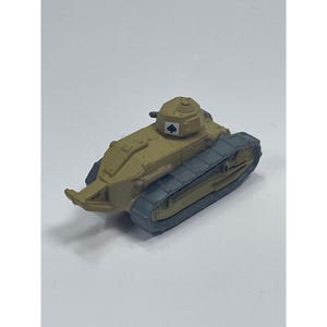 May include: A miniature tan-colored tank model featuring a rotating turret with a small black spade symbol printed on the side. The vehicle has dark gray tracks on both sides and a pointed front section, rendered in a matte finish with molded details.