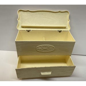 Peut inclure: Une boîte à bijoux en bois blanc avec un couvercle à charnières et un tiroir. La boîte a un motif floral sculpté sur le devant.
