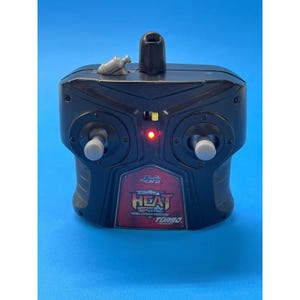 May include: Black remote control with the text "HEAT TURBO" on a red and black label. The remote has two gray control sticks, a small antenna, and a red light. The remote is on a blue background.