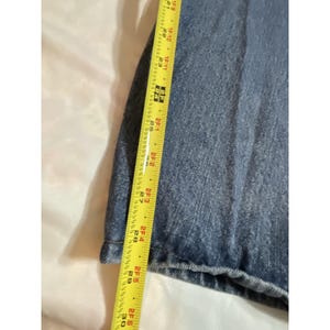 May include: Close-up of blue denim fabric with a yellow measuring tape. The tape shows a measurement of approximately 30 inches. The denim has a classic, faded appearance.