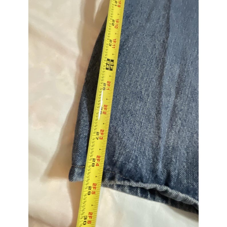 May include: Close-up of blue denim fabric with a yellow measuring tape. The tape shows a measurement of approximately 30 inches. The denim has a classic, faded appearance.