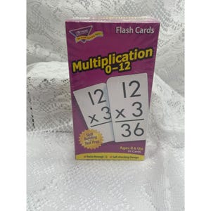 Puede incluir: Una caja morada de tarjetas didácticas de multiplicación 0-12 de Trend. El frente presenta el texto Multiplication 0-12, Skill Building and Test Prep, Ages 8 & Up, 91 Cards, Facts through 12 y Self-checking Design con dos tarjetas.