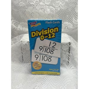 Puede incluir: Una caja azul de tarjetas didácticas de División 0-12 con texto amarillo y tarjetas blancas que muestran problemas de división como 108 dividido por 9 igual a 12. El empaque incluye el texto Skill Building and Test Prep, Ages 9 & Up, 91 Cards y Facts through 12.