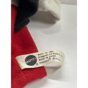 May include: A close-up of a vintage plush toy, featuring red, black, and white fabric. The toy's tag reads "Mattel, Inc. 1993, El Segundo, CA 90245 U.S.A. MADE IN CHINA Disneyland &copy; Disney."