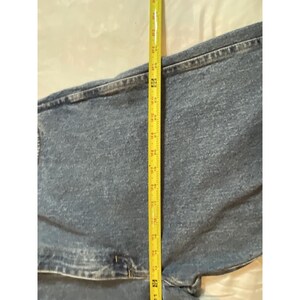 May include: Light blue denim jeans with a yellow measuring tape laid across the garment. The jeans are folded, and the tape shows measurements in inches. The jeans appear to be new.