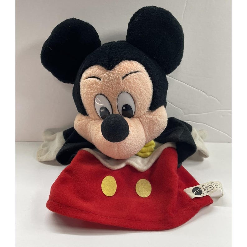 May include: A vintage Mickey Mouse hand puppet. The puppet features a plush black head with large ears, a black nose, and a red outfit with two yellow buttons. The puppet has a white collar and gloves.