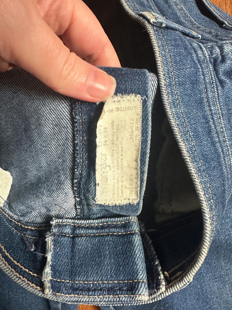 Puede incluir: Primer plano de unos vaqueros azules con una etiqueta blanca. La etiqueta tiene texto y n&uacute;meros, incluyendo la talla 34W 34L. Los vaqueros est&aacute;n hechos de una tela de mezclilla duradera y presentan detalles de costura cl&aacute;sicos.