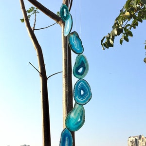 Puede incluir: Un carillón de cristal de ágata azul colgado de una rama de árbol. El carillón está hecho de seis rebanadas de ágata, cada una con un patrón diferente. El carillón está colgado de un anillo de madera.