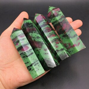 Puede incluir: Cuatro puntas de piedras preciosas verdes y rosas con vetas negras. Las puntas están dispuestas en forma de abanico y se sostienen en una mano.