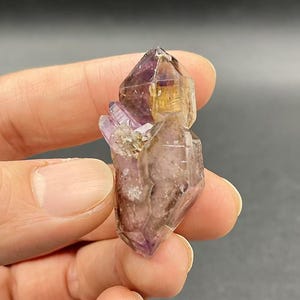 以下が含まれることがあります： 紫と透明な色の変化を見せるアメジストの結晶の塊。結晶は尖っていて、自然で粗い質感です。
