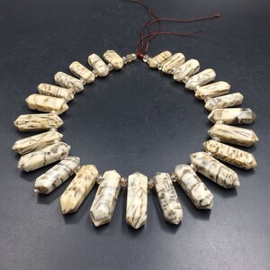 May include: A necklace made of light brown and white agate beads with a pointed shape. The beads are strung on a brown cord and have a natural, organic look.