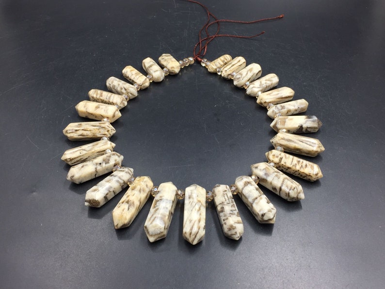 May include: A necklace made of light brown and white agate beads with a pointed shape. The beads are strung on a brown cord and have a natural, organic look.