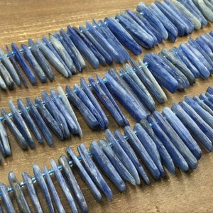 May include: A strand of blue kyanite beads, each bead is a long, thin, and slightly irregular shape. The beads are strung on a thin wire and are arranged in a staggered pattern.