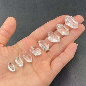 以下が含まれることがあります： 手のひらに置かれた、大きさの異なる7つの透明なダブルターミネーションクォーツポイントのセットです。