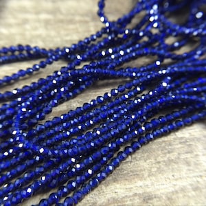 Peut inclure: Un brin de perles facettées bleu foncé. Les perles sont petites et rondes, et elles sont enfilées sur un fil transparent.