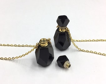 Op de afbeelding: Een ketting met een zwarte glazen fles en een gouden ketting. De fles heeft een facetgeslepen ontwerp en een gouden schroefdop. De ketting wordt getoond met een aparte flesdop.