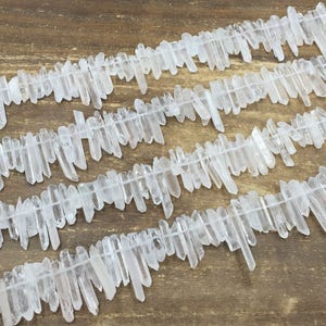 Puede incluir: Una hebra de puntas de cristal de cuarzo blanco, también conocido como cristal de roca, dispuestas en un patrón escalonado. Las puntas son de varias longitudes y están enhebradas en un hilo transparente.