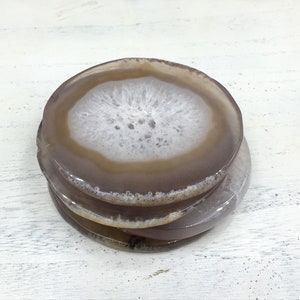 Peut inclure: Ensemble de trois sous-verres en agate brune avec des centres en agate blanche. Les sous-verres sont ronds et ont une finition naturelle et polie.