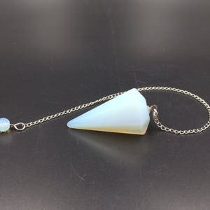 Puede incluir: Un péndulo de ópalo blanco con una cadena de plata. El péndulo tiene forma de pirámide y tiene una pequeña cuenta de plata en el extremo de la cadena.