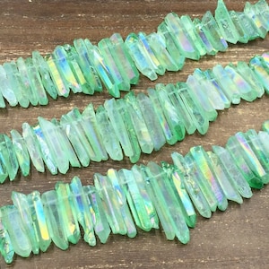 Op de afbeelding: Een streng van regenboogkleurige groene kristallen punten, ook bekend als engel aura kwarts, gerangschikt in rijen op een houten oppervlak.