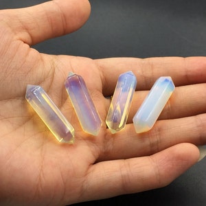 以下が含まれることがあります： 黄色、白、青の様々な色合いの虹色のオパールクリスタルポイントが4つ。ポイントは手のひらに一列に並んでいます。
