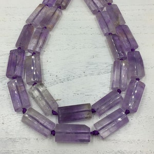 Peut inclure: Un collier de perles d'améthyste violettes, chaque perle est de forme prismatique rectangulaire, avec un cordon violet reliant les perles.