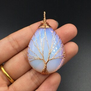 May include: A teardrop-shaped pendant featuring a tree of life design crafted from copper wire wrapped around a white opal stone.