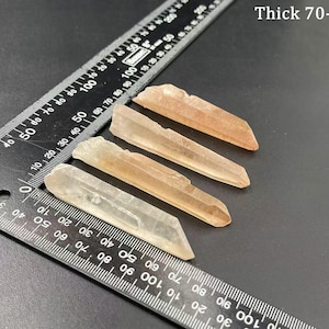 May include: Five clear quartz crystal points with a light pink hue. The crystals are approximately 7 to 8 centimeters in length. A ruler is in the background for size reference.
