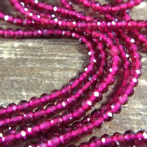 May include: A strand of deep pink faceted glass beads. The beads are small and round, and they are strung together on a clear thread.