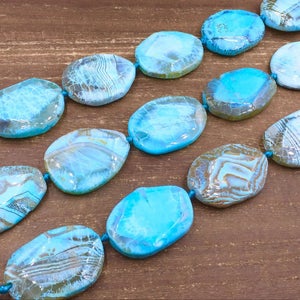 May include: A strand of turquoise blue agate gemstone beads. The beads are oval shaped and have a natural, polished finish.