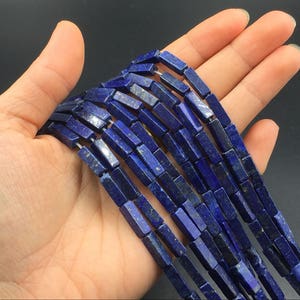 May include: A strand of dark blue lapis lazuli gemstone beads, each bead is a rectangular prism shape.