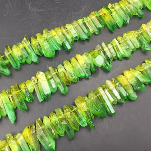 May include: A strand of green and yellow crystal beads. The beads are long and thin, with a pointed end. They are arranged in a row, with the green end of each bead facing the same direction.
