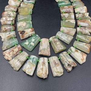 May include: A strand of green and white agate beads, each bead is a different shape and size, with a green thread running through the center of each bead.