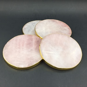 May include: Set of four round pink and white coasters with gold trim. The coasters are made of natural stone and are ideal for protecting surfaces from heat and scratches.