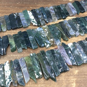 May include: A collection of green, gray, and white agate gemstone sticks. The sticks are various lengths and widths, and have a natural, rough texture.