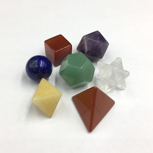 Könnte beinhalten: Satz von sieben geometrischen Kristallformen in verschiedenen Farben, darunter ein klarer Stern, ein violetter Dodekaeder, ein grüner Dodekaeder, ein roter Würfel, eine gelbe Pyramide, eine rote Pyramide und eine blaue Kugel.