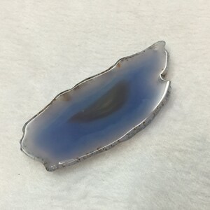 May include: A light blue agate slice with a white and grey banded pattern. The agate is smooth and polished, with a natural, irregular shape.