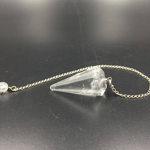 May include: A clear quartz crystal pendulum with a silver chain and a small clear quartz crystal bead at the top.