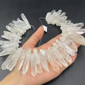 May include: A strand of clear quartz crystal points, also known as rock crystal, arranged in a fan shape. The points are smooth and polished, with a translucent appearance. The crystals are strung on a thin wire, ready for use in jewelry making or other craft projects.
