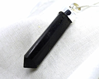 May include: A black, hexagonal, pointed crystal pendant suspended from a silver-toned metal bail. The stone has a smooth, dark surface with subtle natural variations. The pendant is attached to a thin, delicate silver-colored chain necklace.