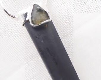 May include: A pendant featuring a long, dark gray, hexagonal stone point capped in silver metal. A smaller, triangular, translucent olive-green stone is set into the silver cap, which is attached to a circular silver bail at the top.