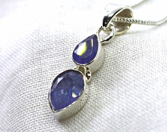 May include: A silver pendant necklace featuring two vertically aligned, pear-shaped, faceted blue gemstones set in polished silver bezels. The pendant hangs from a delicate silver chain, showcasing a reflective surface and deep blue hues.