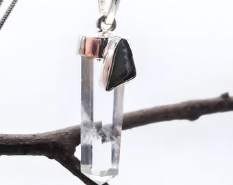 May include: A clear, hexagonal, transparent crystal pendant with a polished silver-toned metal cap. A small, triangular, opaque black stone is attached to the side of the silver cap. The pendant hangs from a thin, silver-toned metal chain.