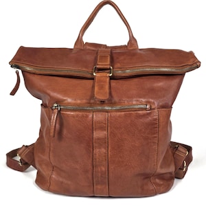 Puede incluir: Una mochila de cuero marrón con cierre enrollable, una correa con hebilla central, un asa superior y un bolsillo frontal horizontal con cremallera. La bolsa incluye correas ajustables para los hombros y herrajes de metal en tono latón antiguo.