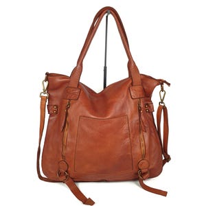 May include: A brown leather tote bag with two handles and a detachable shoulder strap. The bag has two exterior zippered pockets and a large pocket on the back. The bag is made of a distressed leather.