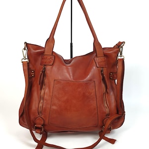 May include: A brown leather tote bag with a front pocket and two zippered compartments. The bag has two top handles and a detachable shoulder strap. The bag is made of a soft, distressed leather.