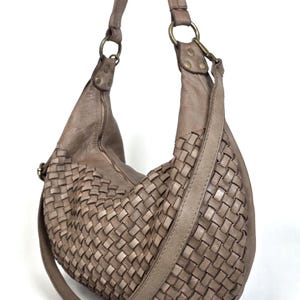 May include: A taupe-colored hobo bag with a woven design on the front. The bag has a long, adjustable strap and a zipper closure. The bag is made of leather and has metal hardware.