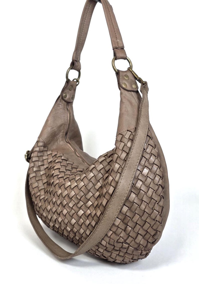 May include: A taupe-colored hobo bag with a woven design on the front. The bag has a long, adjustable strap and a zipper closure. The bag is made of leather and has metal hardware.